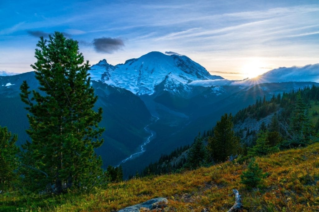 The sun sets behind a snow covered Mount Rainier in the distance in Mount Rainier National Park in Washington