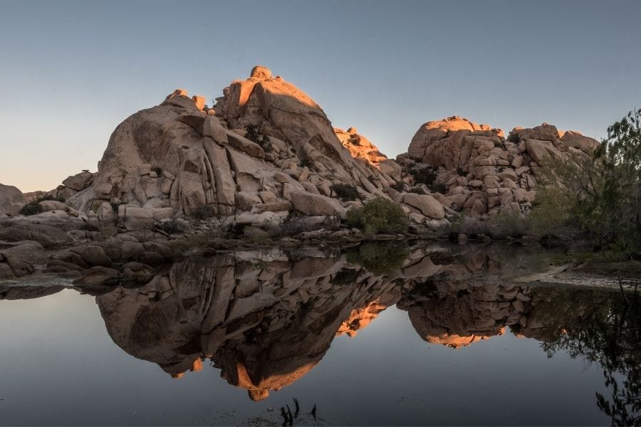 Rocks are reflected in the water of Barker Dam at sunrise