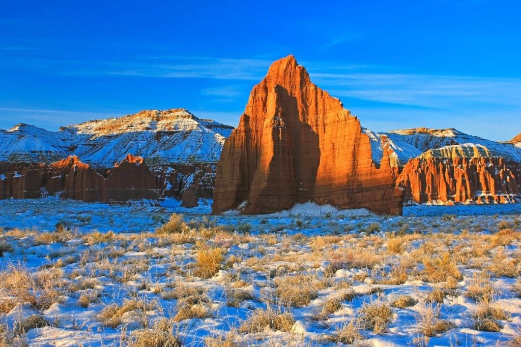 Snow on the ground in front of a red rock spire in Capitol Reef National Park during winter