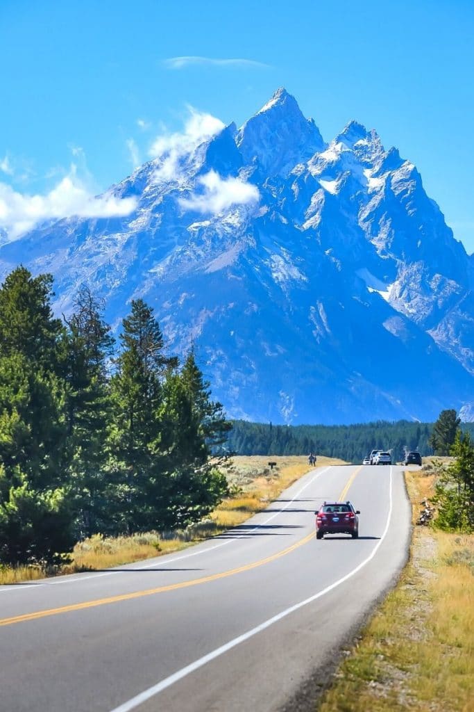 Car drives along Teton Park Road towards the Grand Teton range