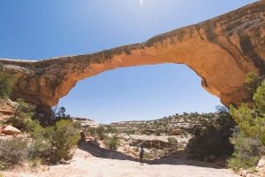 A female hiker walks underneath a natural bridge in Utah in this hiking for beginners guide.