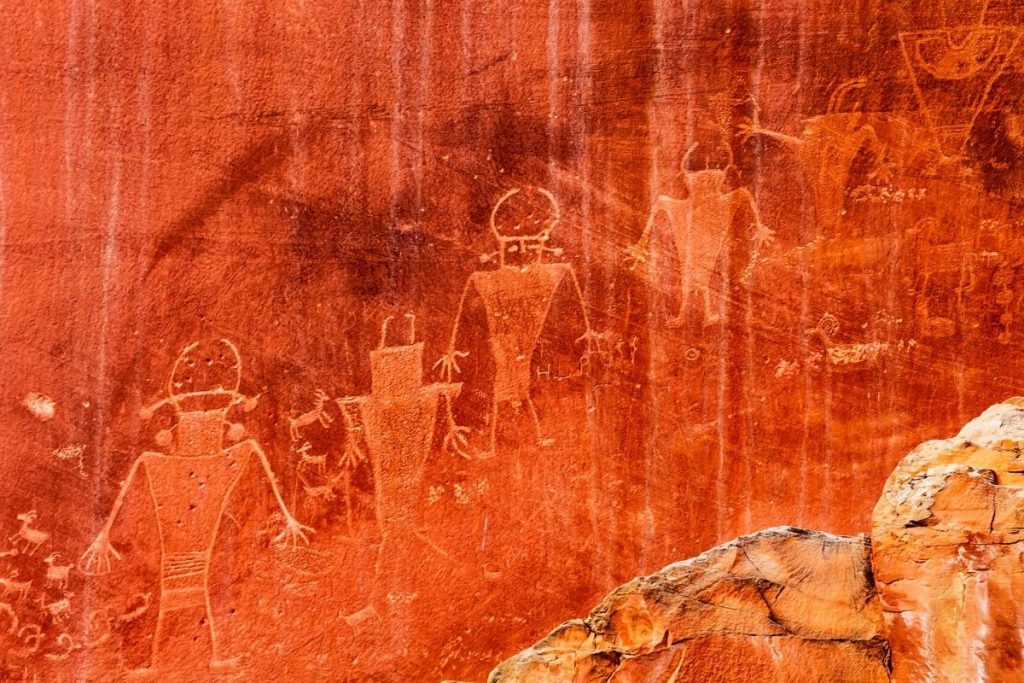 Ancient human figure petroglyph drawings on a red rock wall