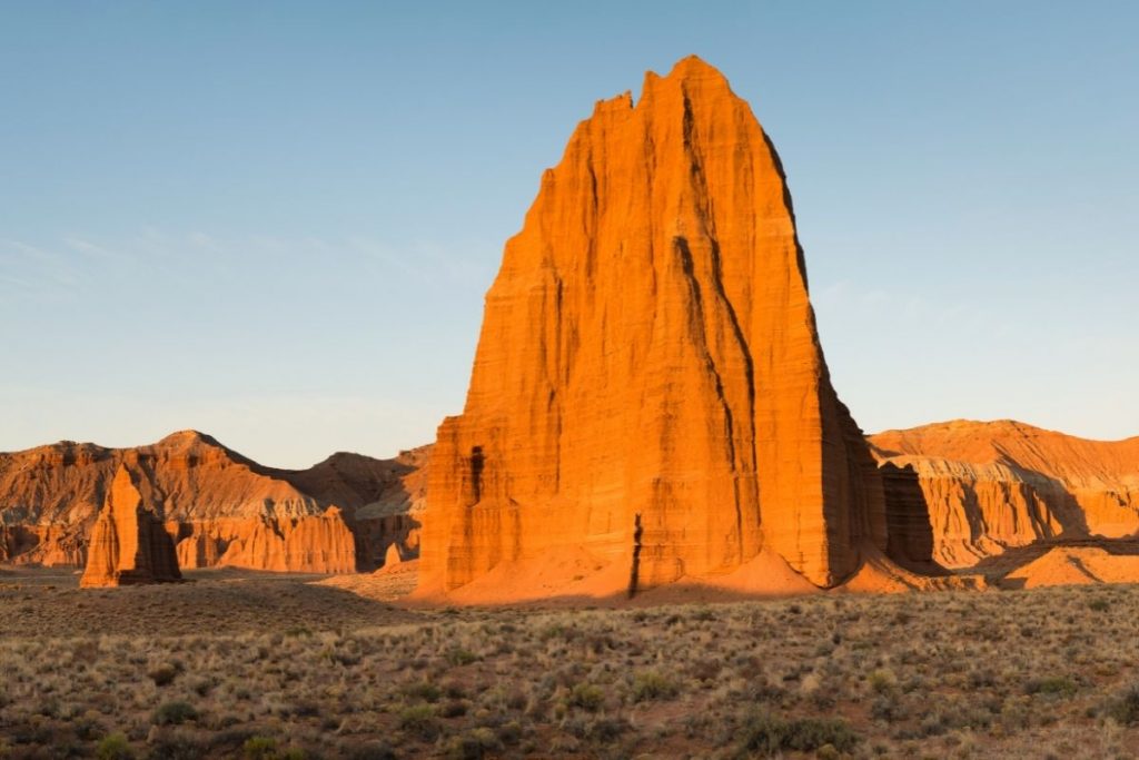 Sunrise makes the tall red rock spire glow fiery orange at Temple of the Sun in Capitol Reef